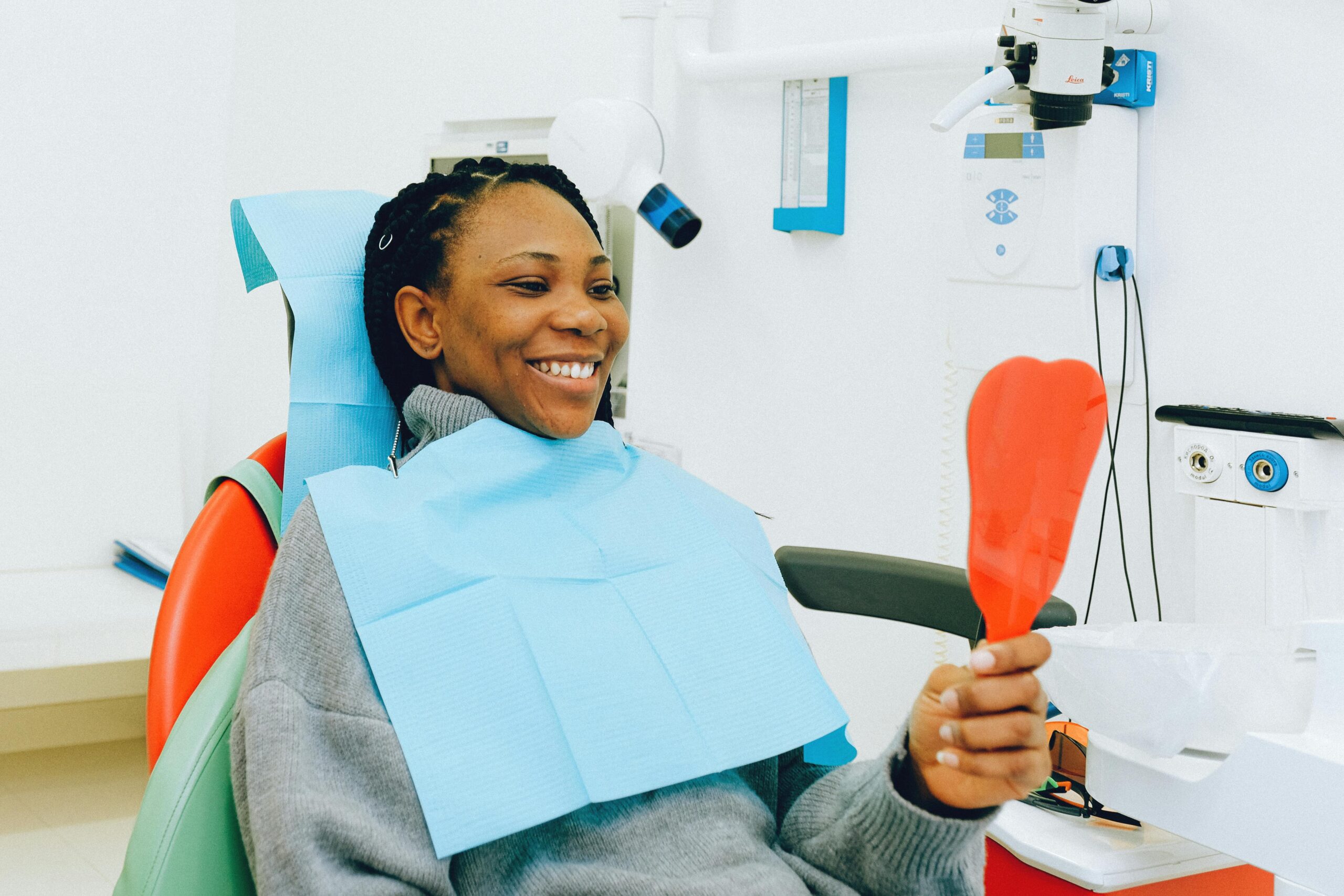 Smiling woman in a dental chair holding a tooth-shaped mirror, possibly after a tooth bonding procedure.